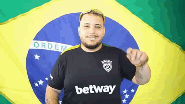 a man wearing a shirt that says ' betway ' on it stands in front of a brazilian flag