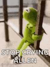 kermit the frog is sitting on a railing holding onto a pole .