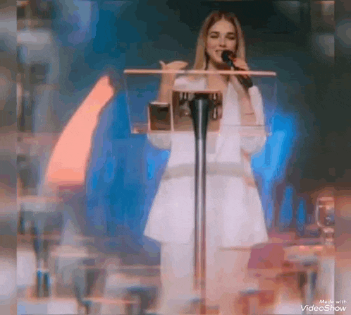 a woman is standing at a podium holding a microphone and singing .