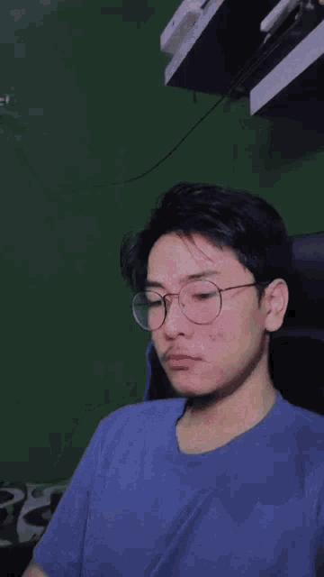 a young man wearing glasses and a blue shirt is sitting in a chair