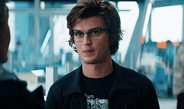 a young man wearing glasses and a black shirt is standing in a room .