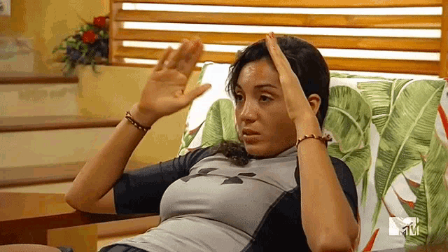 a woman is sitting on a couch with her hands on her head and a mtv logo behind her