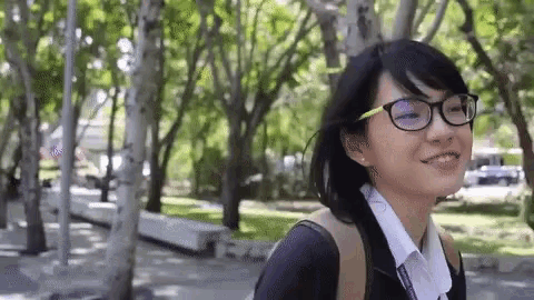 a young woman wearing glasses and a backpack is smiling while walking in a park .