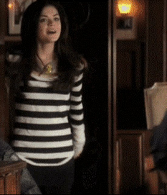 a woman wearing a black and white striped shirt stands in a dark room
