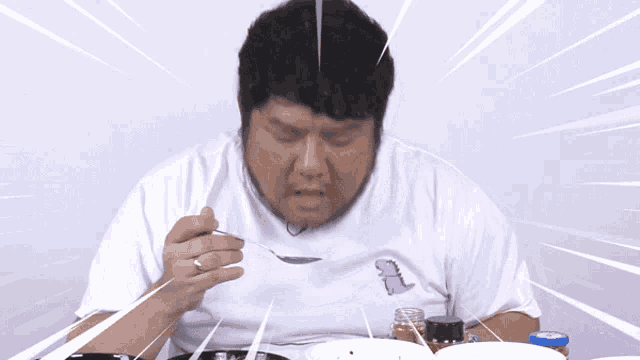 a man wearing a white shirt with a dinosaur on it is eating food with a spoon