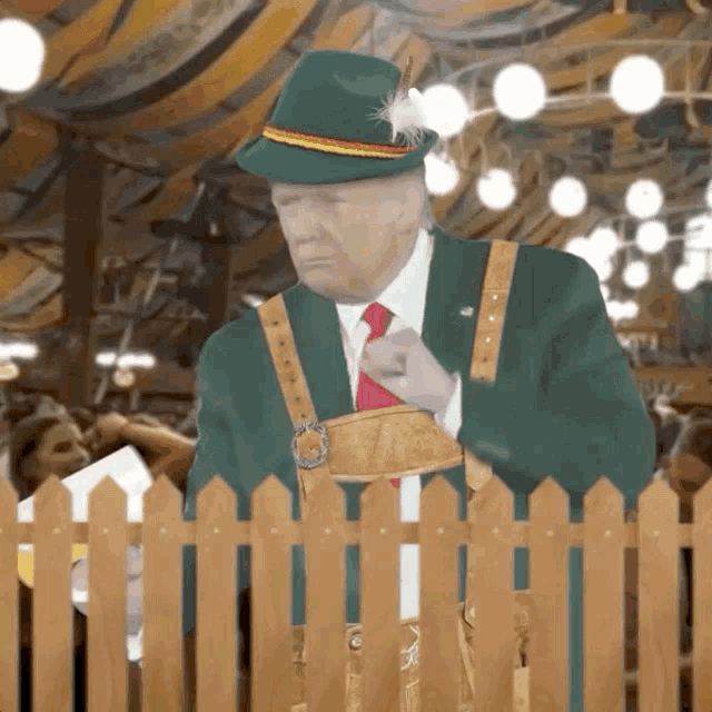 a man in a green hat is standing behind a wooden picket fence