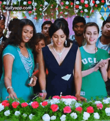 a group of women are standing around a table with flowers and a cake .