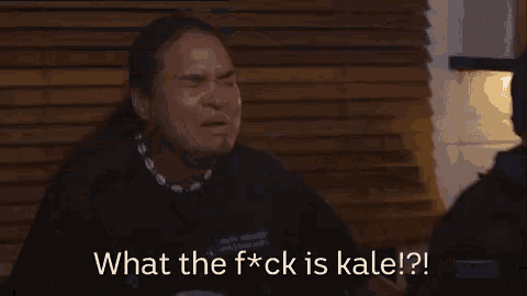 a woman is crying while sitting in front of a wooden wall and says `` what the f * ck is kale ? ''