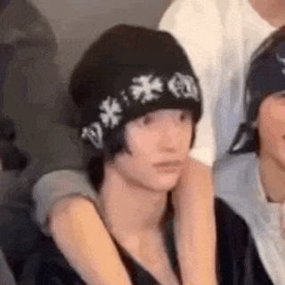 a person wearing a black beanie with white crosses on it is sitting in a crowd of people .