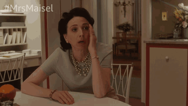 a woman sitting at a table pointing at the camera with the hashtag #mrsmaiset behind her