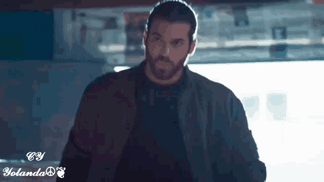 a man with a beard is wearing a black shirt and a brown jacket