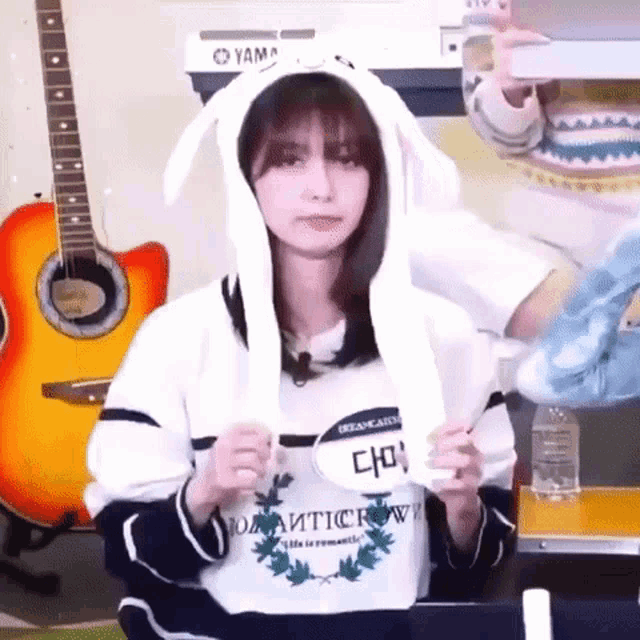 a girl wearing a bunny ear hoodie is holding a sign that says ' cho ' on it .