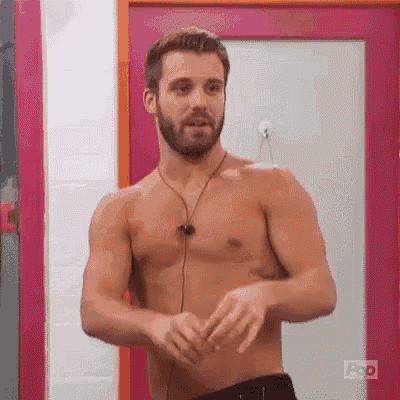 a shirtless man with a beard is standing in front of a pink door in a room .
