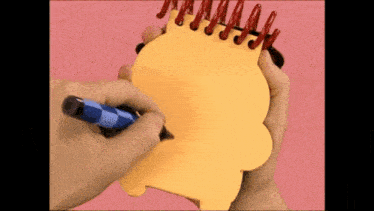 a person is writing in a yellow notebook with a blue marker