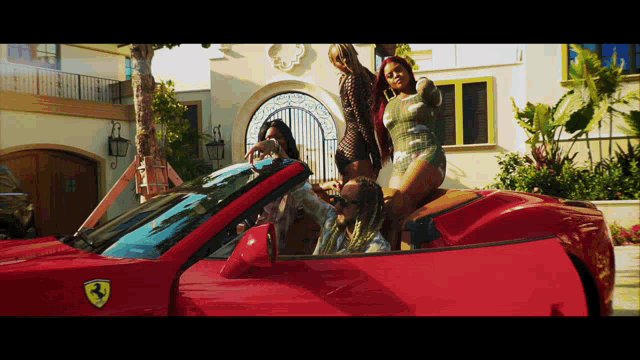 a group of women are standing on top of a red ferrari