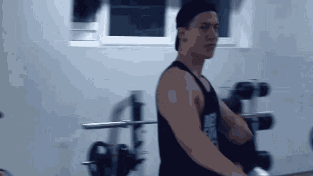 a man in a black tank top is standing in a gym holding a barbell .
