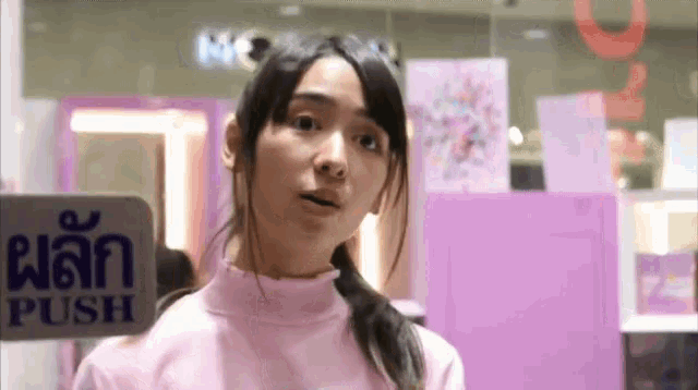 a woman in a pink sweater is standing in front of a sign that says rush