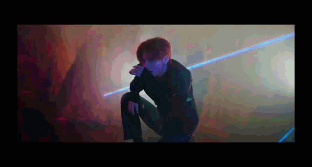 a man is kneeling down in a dark room with a laser beam behind him