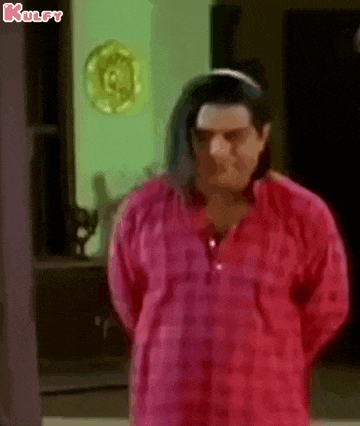 a man in a red shirt is standing in a room with his arms behind his back .