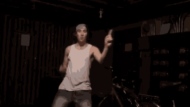 a man in a white tank top and hat is dancing in a dark room .