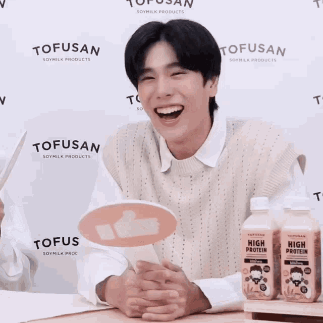 a man is holding a thumbs up sign in front of two bottles of tofusan high protein