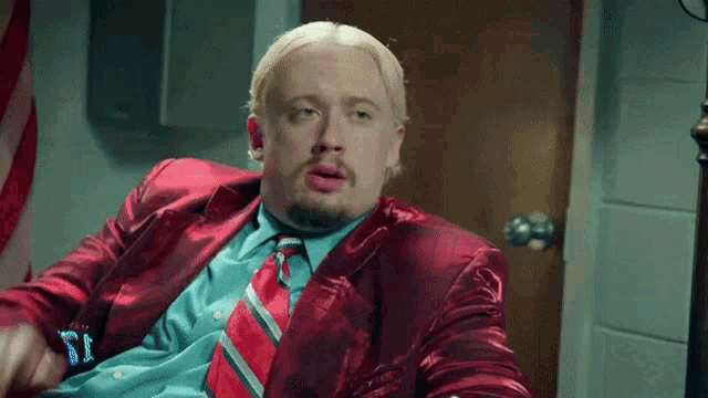 a man with blonde hair and a beard wearing a red jacket and tie