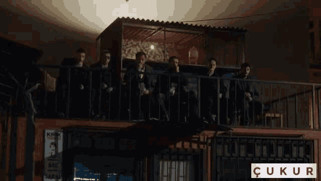 a group of men are sitting on a balcony with a sign that says kirk