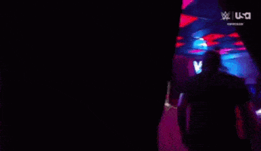 a man in a black shirt is walking through a dark room with a sign that says wwe on it .