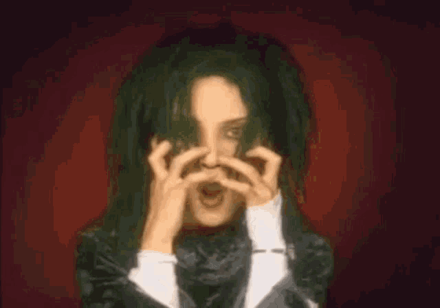 a woman with green hair is covering her face with her hands and making a scary face .