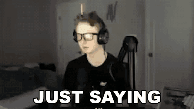 a man wearing headphones and glasses is sitting in front of a microphone and says `` just saying '' .