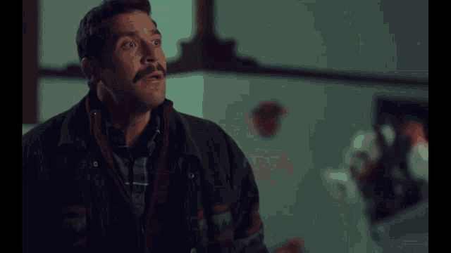 a man with a mustache is wearing a black jacket and a plaid shirt