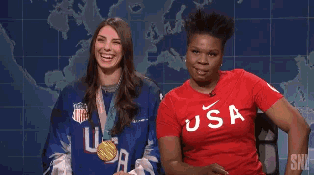 two women are sitting next to each other on a stage . one of the women is wearing a gold medal .