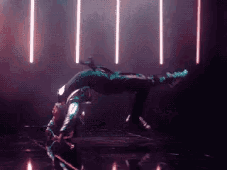 a person is doing a handstand in a dark room with lights behind them