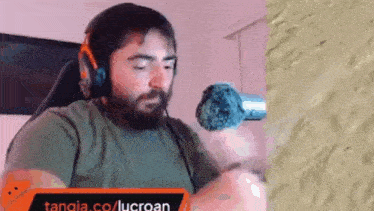 a man with a beard wearing headphones and a microphone is sitting in front of a wall .