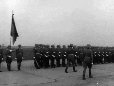 a black and white photo of a military parade with a flag in the foreground
