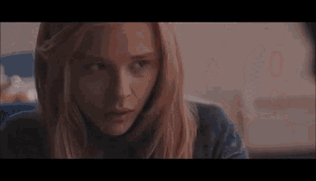a close up of a woman 's face with long blonde hair and a blue shirt .