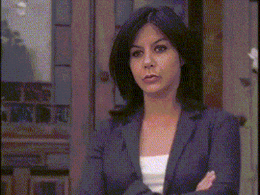 a woman in a suit is standing in front of a door and looking at the camera
