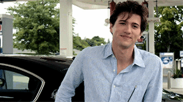 a man in a blue shirt is standing next to a car