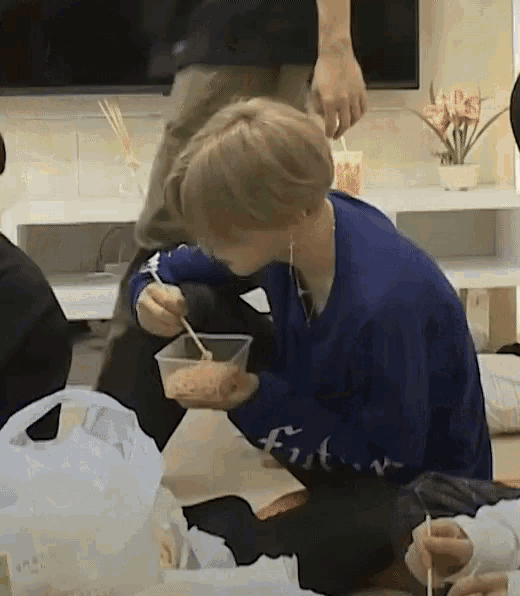 a person in a blue sweater is eating food with chopsticks