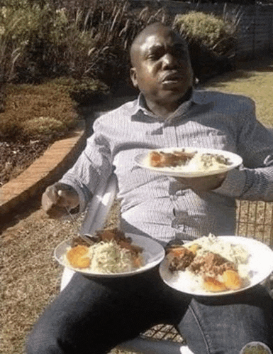 a man is sitting in a chair with two plates of food in his hands .