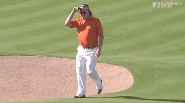 a man wearing an orange shirt and white pants is walking on a golf course sponsored by the european tour