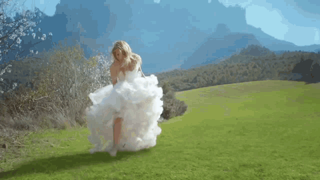 a woman in a white dress is running through a grassy field with mountains in the background