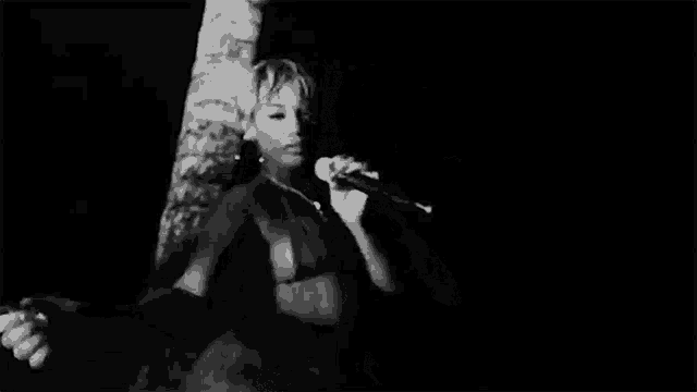 a black and white photo of a woman singing into a microphone while standing in front of a palm tree .