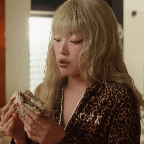 a woman wearing a leopard print jacket holds a sandwich