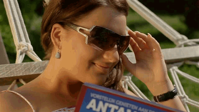 a woman wearing sunglasses is holding a book that says " anta "
