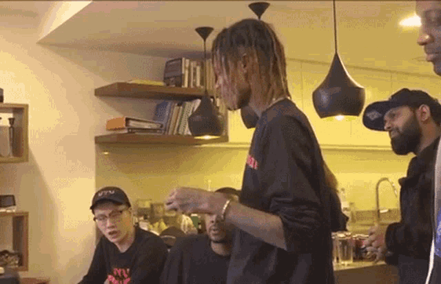 a man with dreadlocks is standing in a kitchen with other men