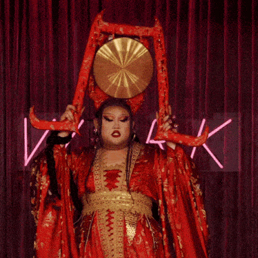 a woman in a red and gold dress is holding a large gong in front of a neon sign that says vilook