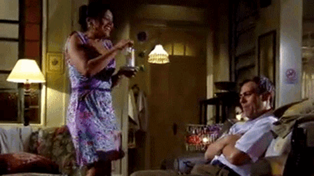 a woman is standing next to a man who is sitting on a couch in a living room .