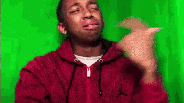a man in a red hoodie is making a funny face in front of a green background .