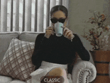 a woman is sitting on a couch drinking from a cup with the word classic on it